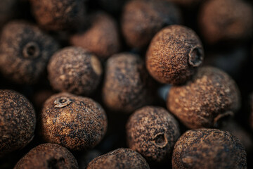 Close-up macro view of dried allspice berries, showcasing their textured surface and earthy brown...