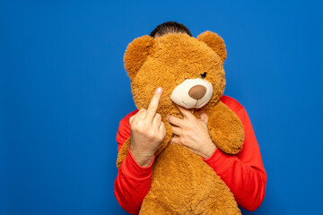 Hispanic man in his 40s holding a teddy bear making a fuck you gesture to the camera, isolated on...