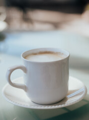 Delicious cappuccino coffee served in a white cup on a glass table.