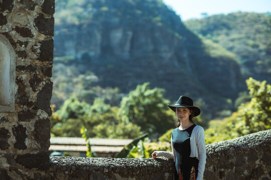 Girl with hat enjoying the view of the mountain landscape from a stone bridge in the magical town of Malinalco, State of Mexico.