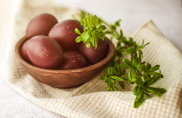 Easter burgundy eggs in a clay plate on a white napkin, decorated with green willow branches on a light background, soft selective focus. Festive background with Easter symbols