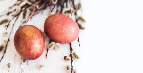 Two red Easter eggs and spring fluffy willow branches on a wooden white surface, copy space, soft focus. Easter background with holiday symbol