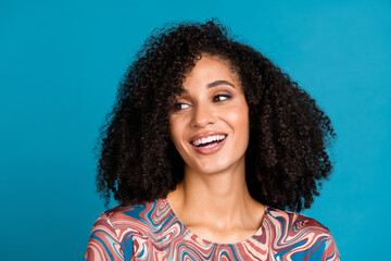 Smiling young woman with curly hair, wearing a trendy print t-shirt, poses against a bright blue background