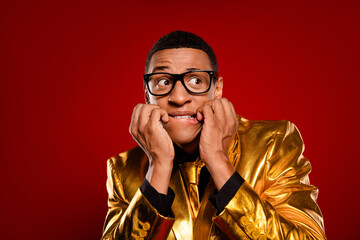 Charismatic young man in a golden suit against a red background, expressing a playful and nervous...