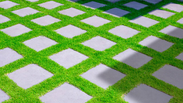 Gray square cobblestone tile floor decoration and green grass on pavement in front yard at home with sunlight and shadow on surface, high angle view with copy space