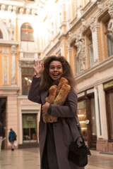 Fototapeta premium A beautiful girl in a coat walks around the city, holding a loaf of bread in her hands