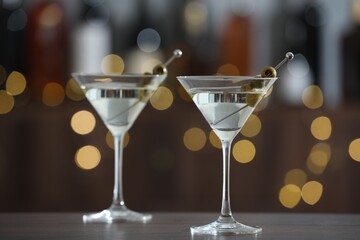 Martini cocktail with olives in glasses on wooden table against blurred background. Bokeh effect