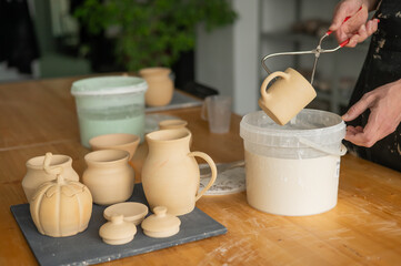 Close-up of a potter's hands glazing a ceramic mug. 