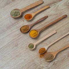 Spices in wooden spoons on wooden background