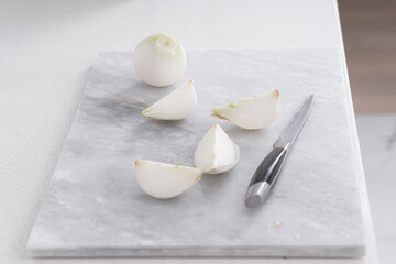 A white onion cut into quarters. A knife lies nearby