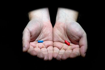 Choose your destiny concept. Male hands holding red and blue pills capsules on black background
