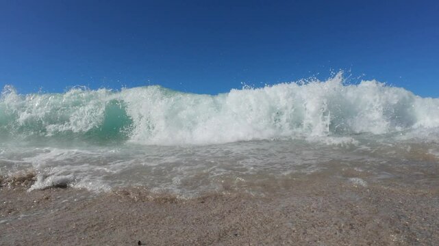 A slow motion video of a wave crashing on the beach and camera