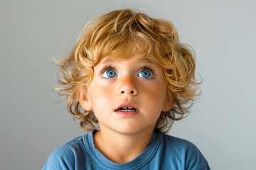 Naklejka premium Curious young child with blonde curls and blue eyes looking upward