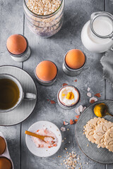 Boiled brown eggs in gray egg cups and other breakfast ingredients on gray background