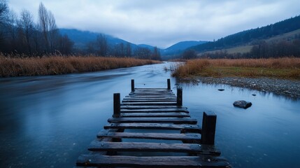 Obraz premium A wooden bridge spans a river in a foggy, misty landscape