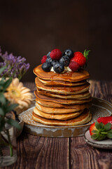 American pancakes with blueberries, strawberries and raspberry on a plate on a dark background