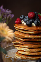 American pancakes with blueberries, strawberries and raspberry on a plate on a dark background