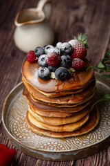 American pancakes with blueberries, strawberries and raspberry on a plate on a dark background