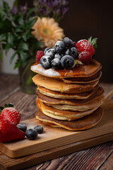 American pancakes with blueberries, strawberries and raspberry on a plate on a dark background