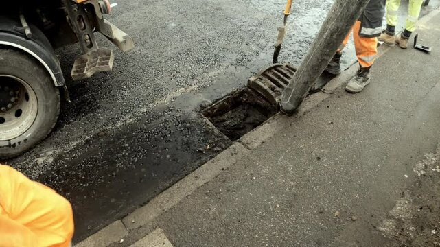 Workers repair street drainage system in urban area during daylight hours