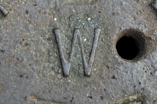 Letra "W" en una Alcantarillado.  Es algo antiguo en Puerto Rico. El material es de metal y est&aacute; un poco corro&iacute;do con el tiempo. 