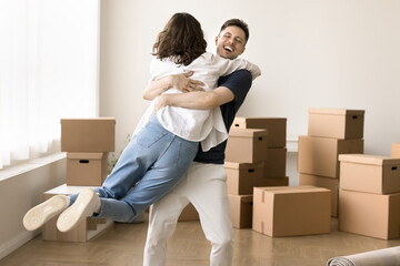 Overjoyed loving couple having fun celebrate moving day. Husband lifting his beloved wife, swirl,...
