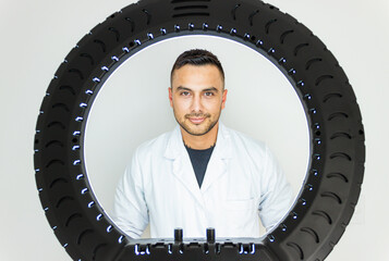 Young Colombian doctor wearing a lab coat and looking at the camera on a white background and a...