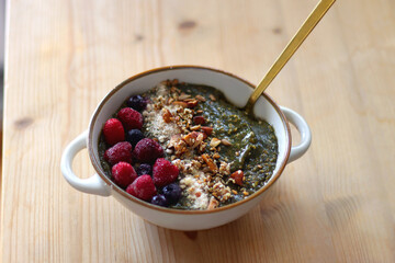 Beige bowl with green smoothie, frozen berries and homemade granola, served on the table. Selective focus.