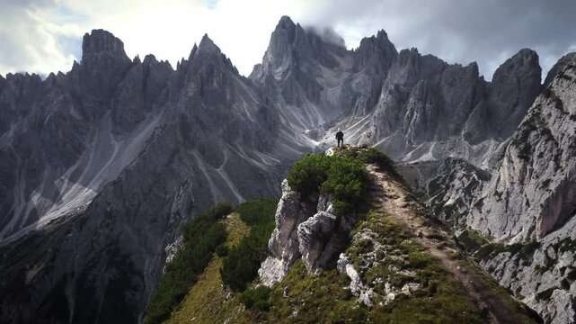Drohnen Luftaufnahme einer Person, die am Rand eines Berges steht, im Hintergrund eine Bergkette in den Dolomiten.
