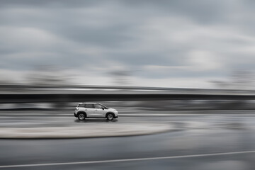 A car is driving on a road in the rain. A fast moving gray car on a speed blurred background