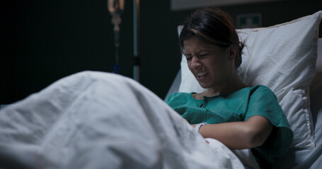 Female patient in hospital ward lying in bed suffering from gastritis.