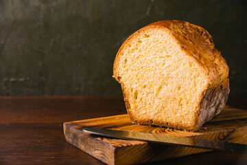 Sweet brioche bun cut on a wooden cutting board and bread knife. Delicious home baked goods