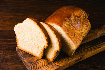 Delicious and sweet buttery bread cut into slices on a dark wooden cutting board. Delicious home baked goods