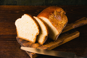 Sweet brioche loaf cut into slices on a wooden cutting board and a bread knife. Delicious homemade pastries