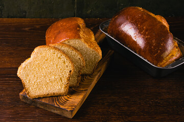 Delicious and sweet buttery bread roll cut into slices on a dark wooden cutting board and a brioche...