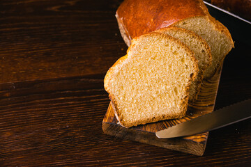 Delicious and sweet buttery bread cut into slices on a dark wooden cutting board. Delicious home baked goods