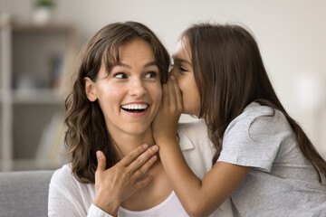 Close up of little daughter telling secret in moms ear, share funny joke, or prepared surprise, explain exciting plans on weekend, making heartfelt confession at home. Trust between parent and child