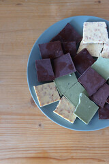 Plate with dark, white and matcha chocolate pieces. Top view, wooden background.