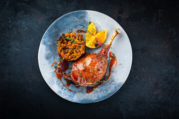 Traditional barbecue gourmet duck haunch with mushroom risotto and orange slices served with spicy chili sauce as top view on a design plate 