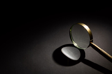 Old vintage gold magnifying glass with shadow on dark background under beam of light