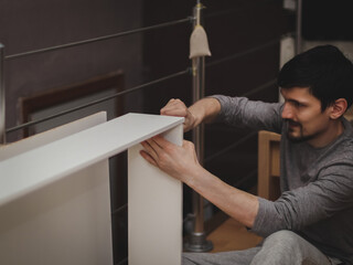 A man tightens screws with a screwdriver while assembling furniture.