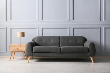 Stylish sofa and lamp on side table near grey wall
