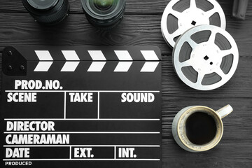 Movie clapper, camera lens, film reels and cup of coffee on black wooden table, flat lay
