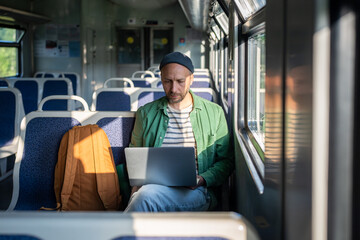 Man works on laptop during morning commute on train, remote freelance with WiFi in public...