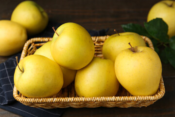 Fresh yellow apples in wicker basket on table, closeup