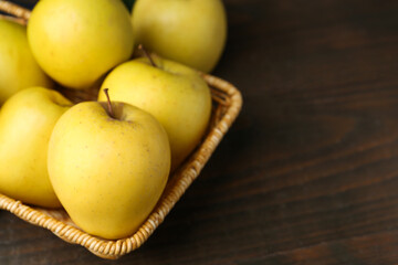 Fresh yellow apples in wicker basket on wooden table, closeup. Space for text