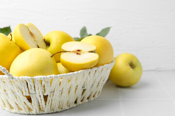 Fresh ripe yellow apples in basket on white tiled table, closeup. Space for text