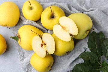 Fresh ripe yellow apples and green leaves on grey table, above view