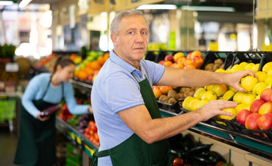 in department of vegetables and fruits, man seller chooses ripe and sweet apples for buyer