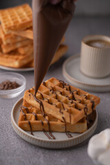 photo Delicious golden waffles drizzled with rich chocolate sauce served with a steaming cup of coffee, perfect for a hearty breakfast or a delightful snack